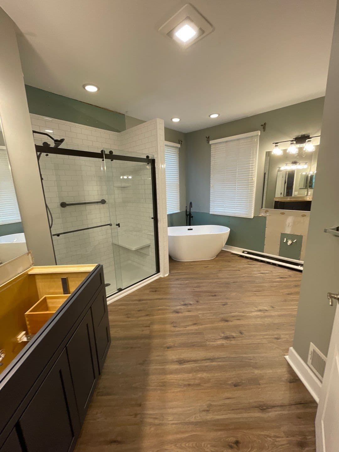 A gray bathroom with a walk-in shower with sliding glass doors, built-in shower bench, and grab safety bar on the left, and a large soaking bathtub on the right in the far corner.