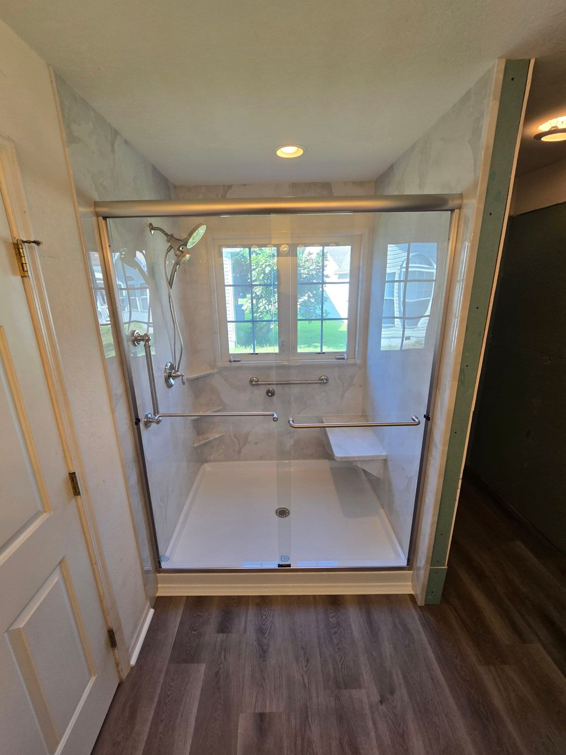 A new walk-in acrylic shower with sliding glass doors, built-in bench seat, grab bar, and window.