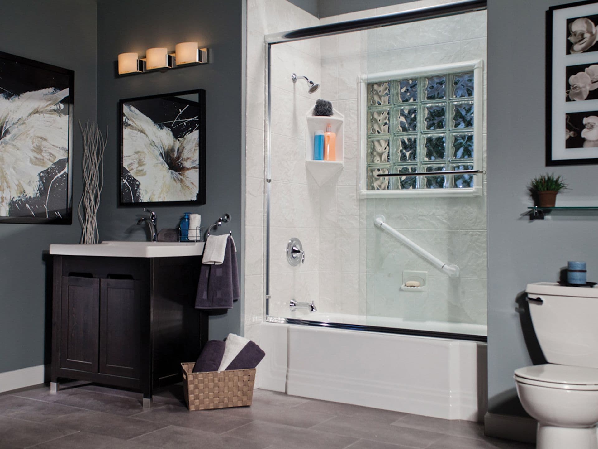 A gray bathroom with a combination shower-tub with a window, sliding glass doors, corner shelves and diagonal grab bar.