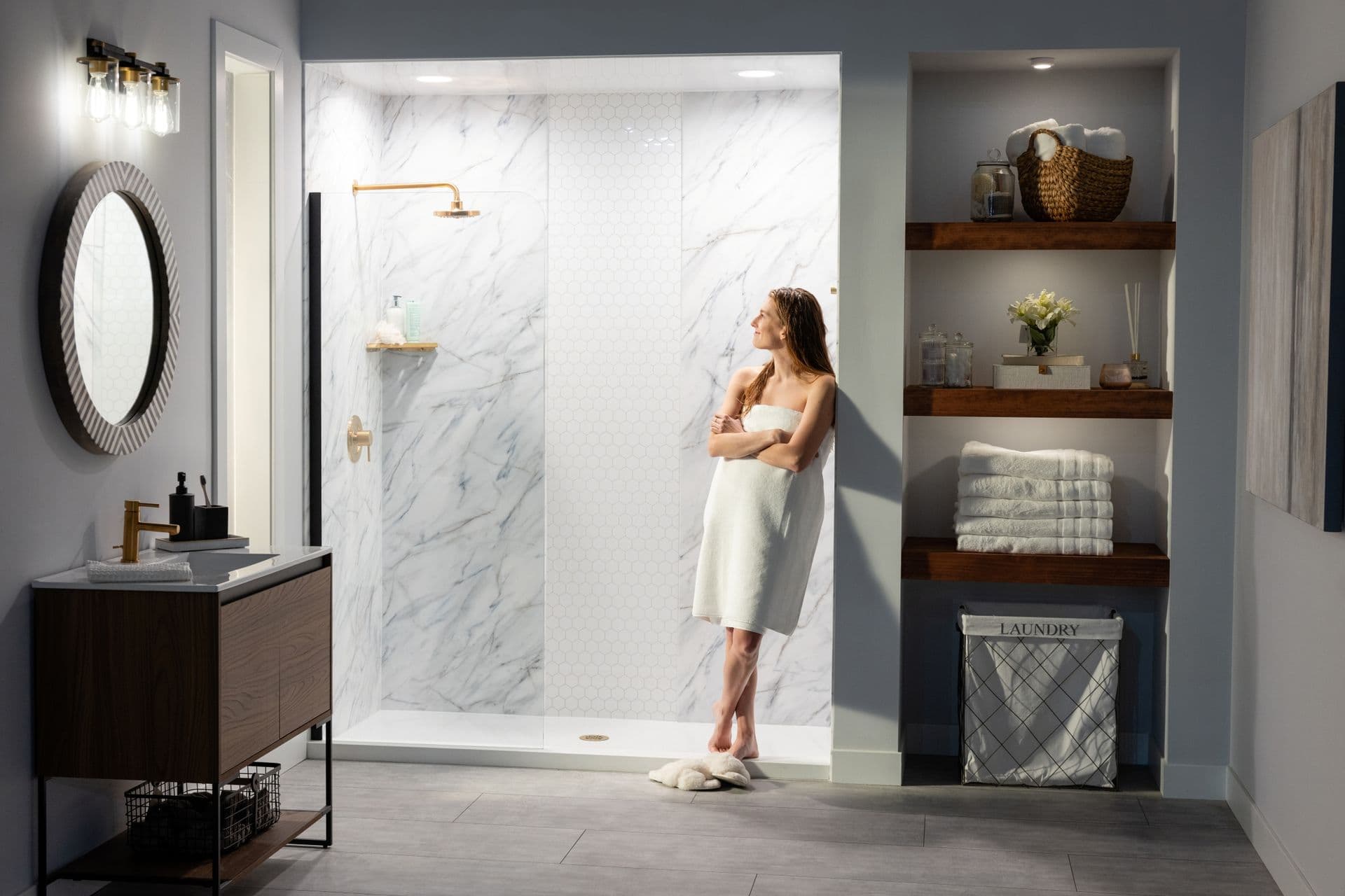 A person stands in a gray bathroom outside a newly renovated walk-in shower with gold fixtures.
