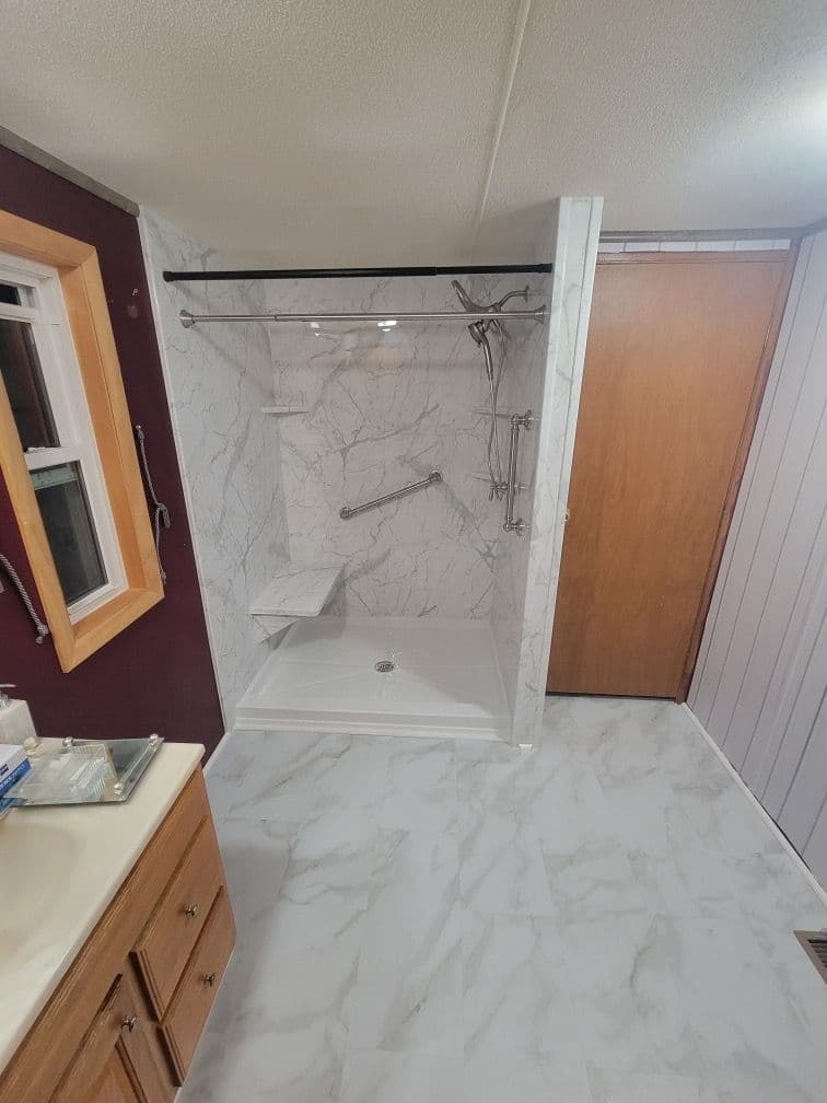 A remodeled bathroom with walk-in shower with gray and white marbled walls, built-in shower bench, and diagonal grab bar.