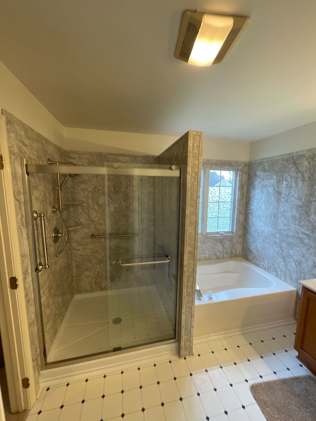 A bathroom with beige marbled walls and a walk-in shower with sliding glass doors on the left and a large soaking bathtub on the right.