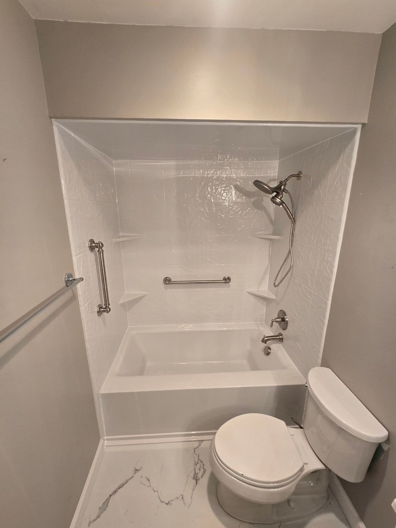 A remodeled combination shower tub with white, textured walls, vertical and horizontal grab bars, and corner shelves.