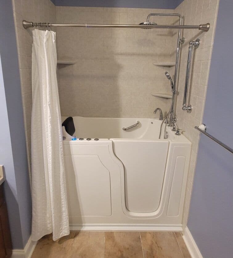 An accessible walk-in bathtub and shower with corner shelves in a light blue bathroom.