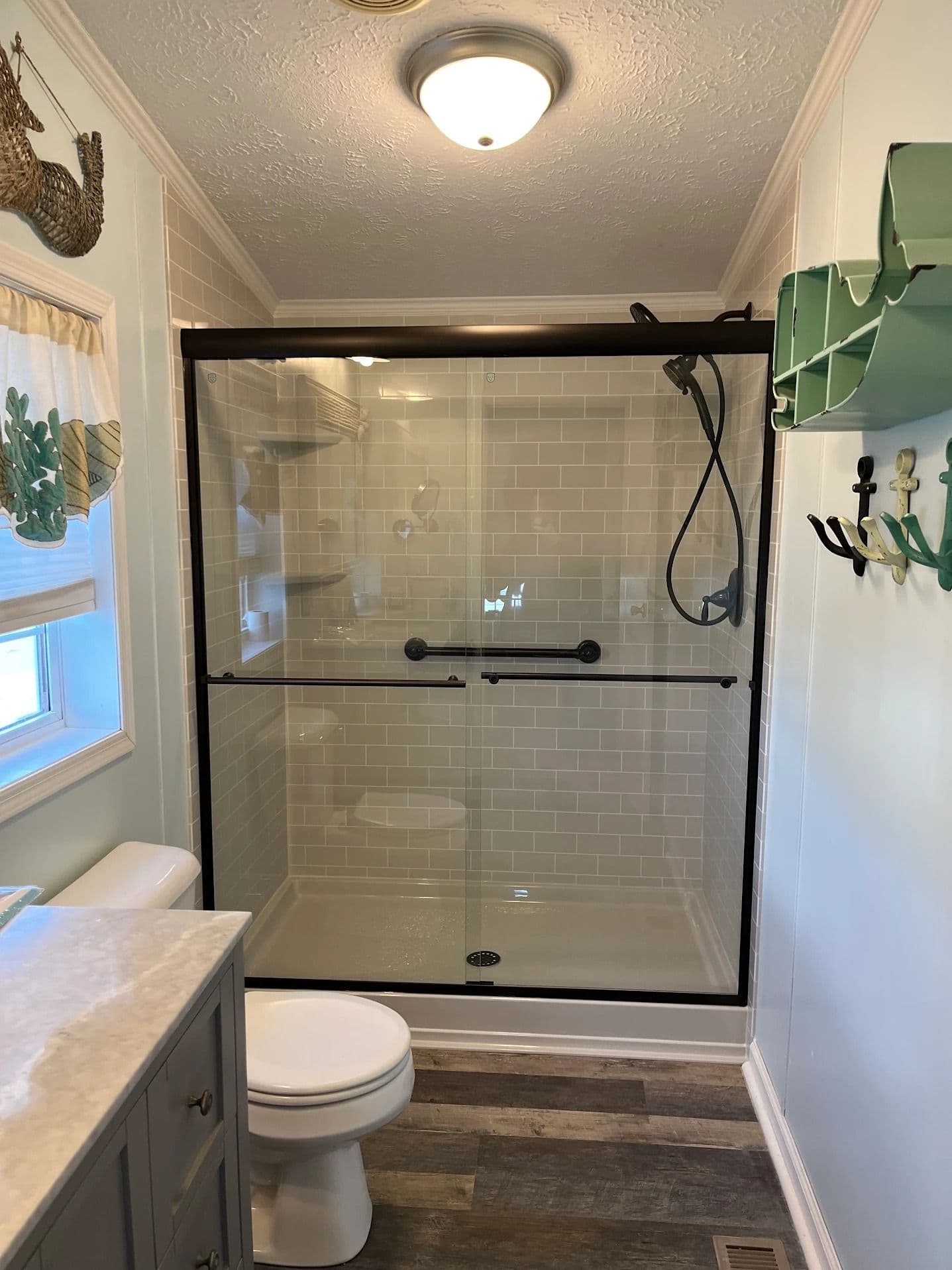 A walk-in shower with sliding glass doors, black fixtures, safety grab bar, and beige tile patterned walls.