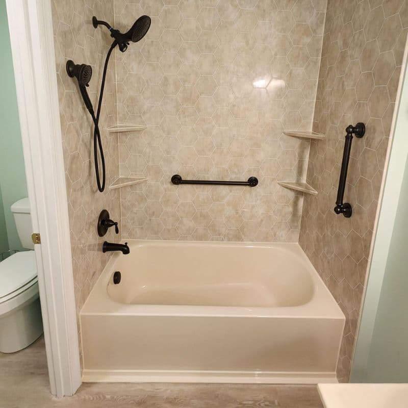 A combination shower tub with beige hexagonal tile pattern walls, black fixtures, and grab bars.