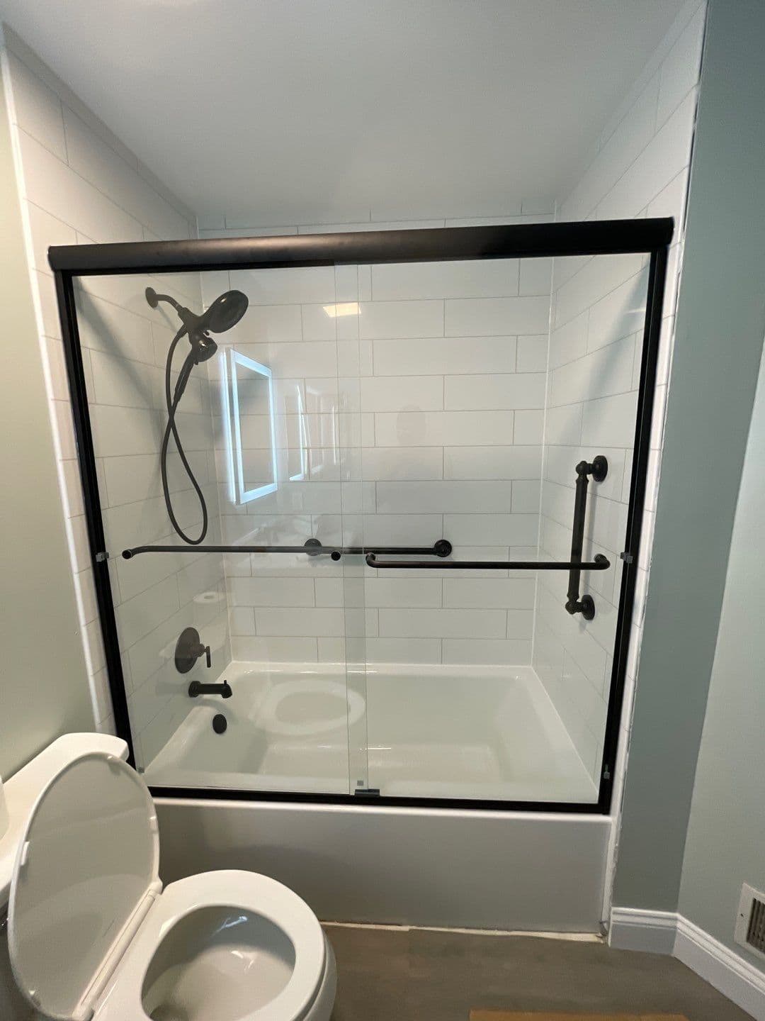 A combination shower tub with sliding glass doors, black fixtures, and grab bars.