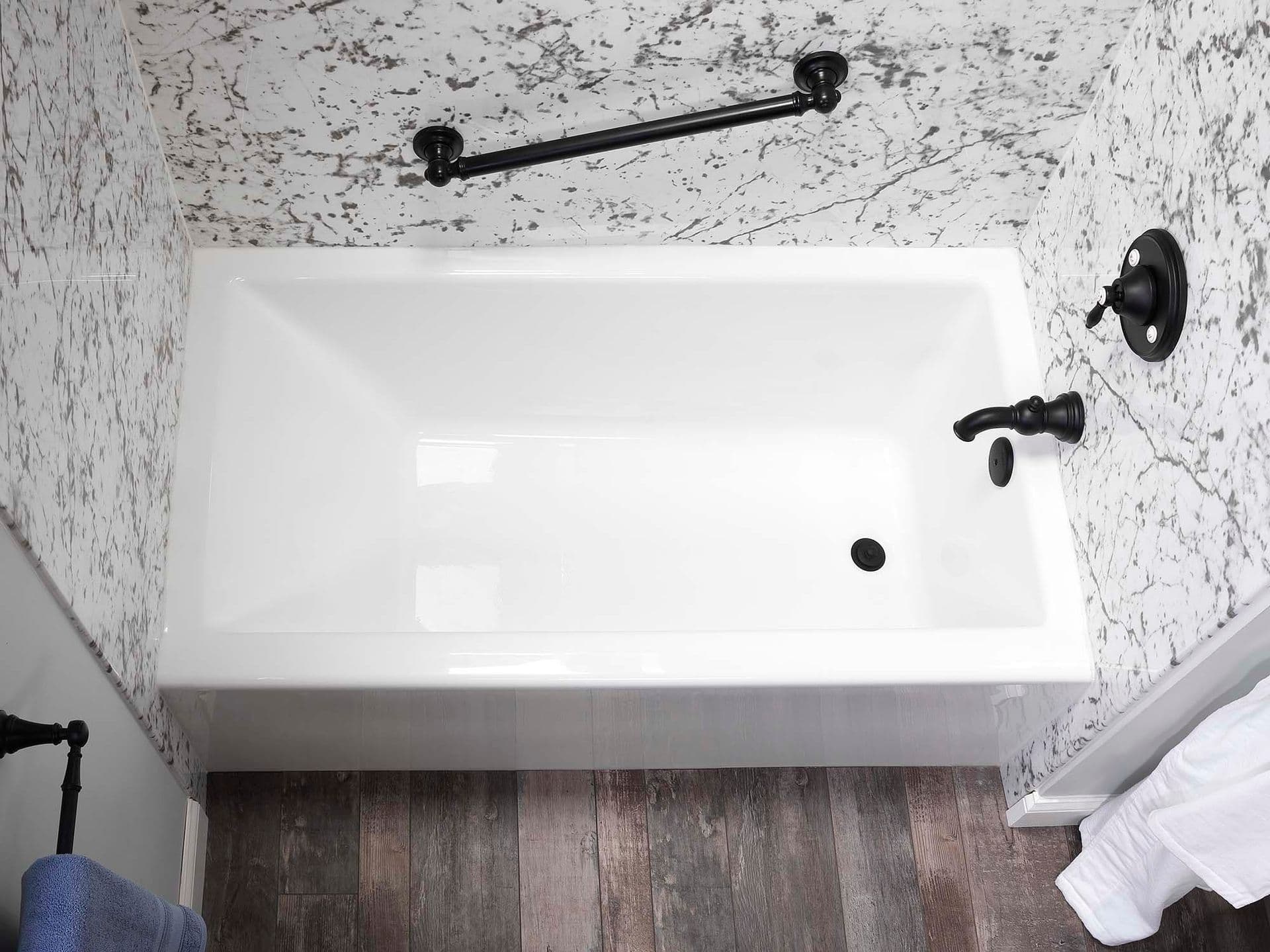 A top-down view of a new white bathtub with matte black fixtures and gray and white marbled walls.