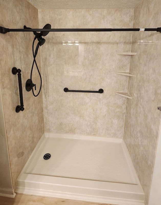 A walk-in shower with a vertical grab bar and horizontal safety bar.