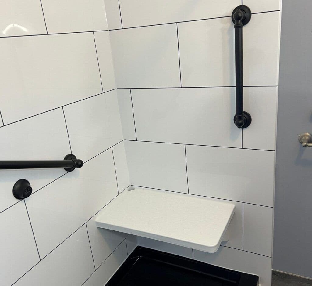 An accessible shower with built-in shower seat bench and matte black grab bars.