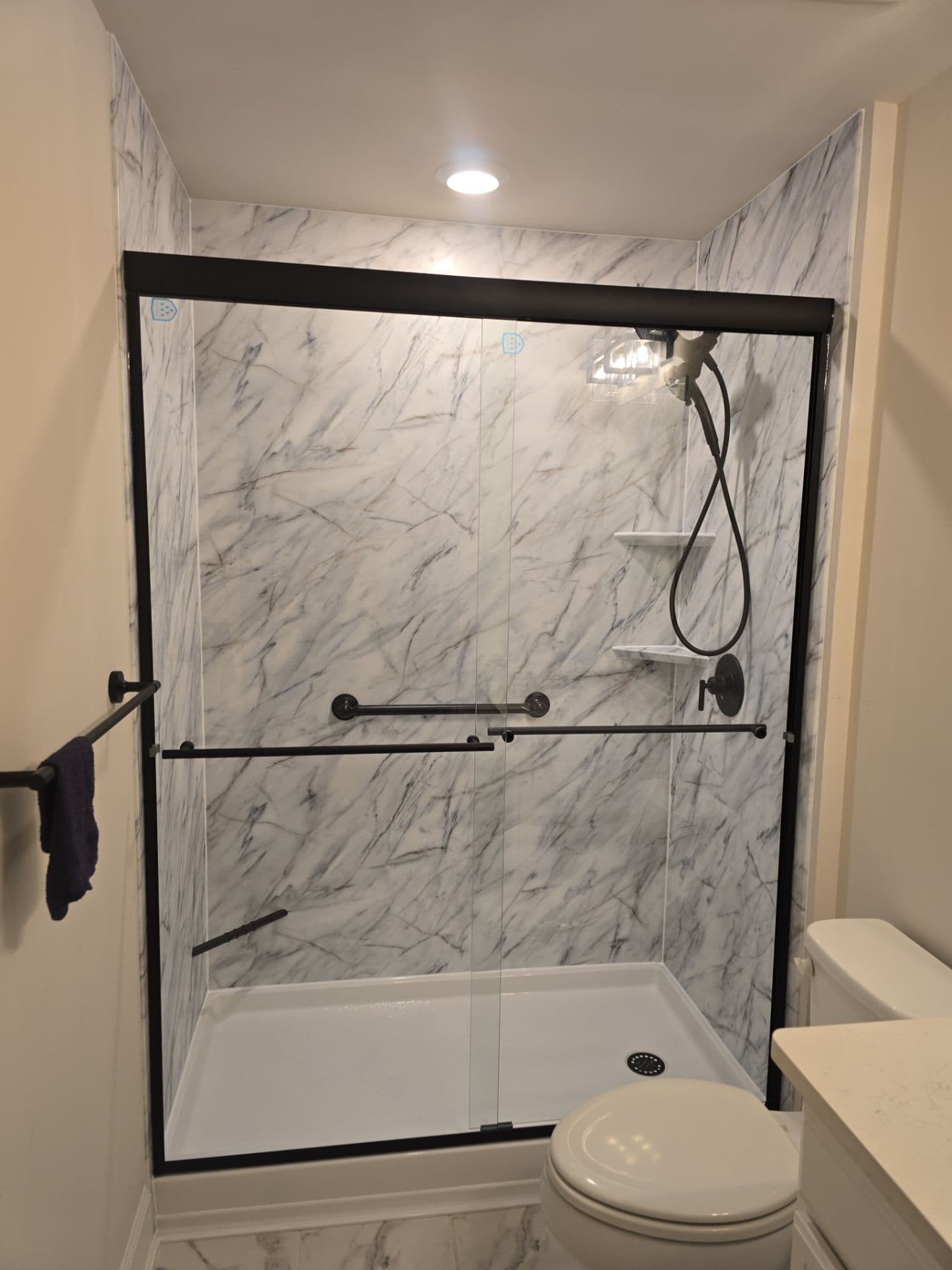 A gray and white marbled walk-in shower with sliding glass doors and corner shelves.