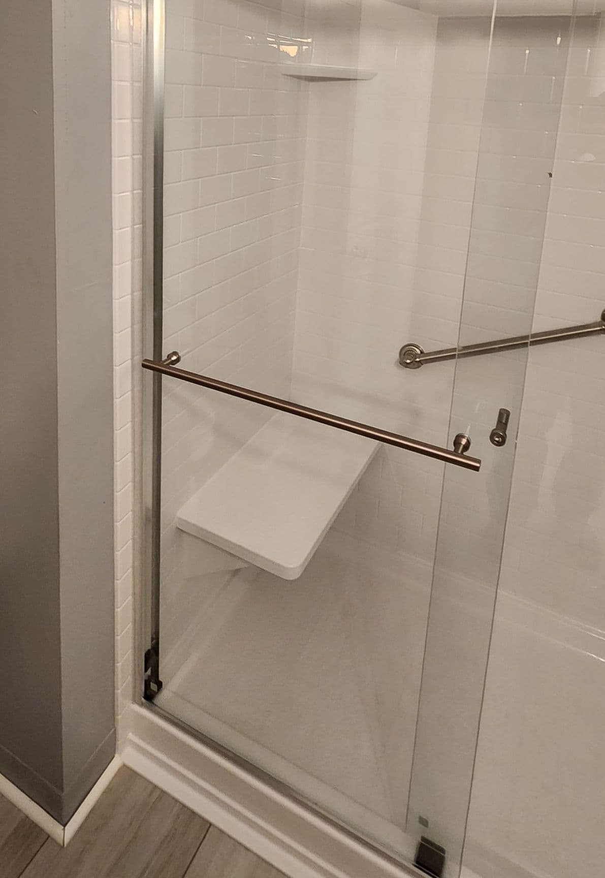 A walk-in shower with shower bench, sliding glass doors, and grab bar.