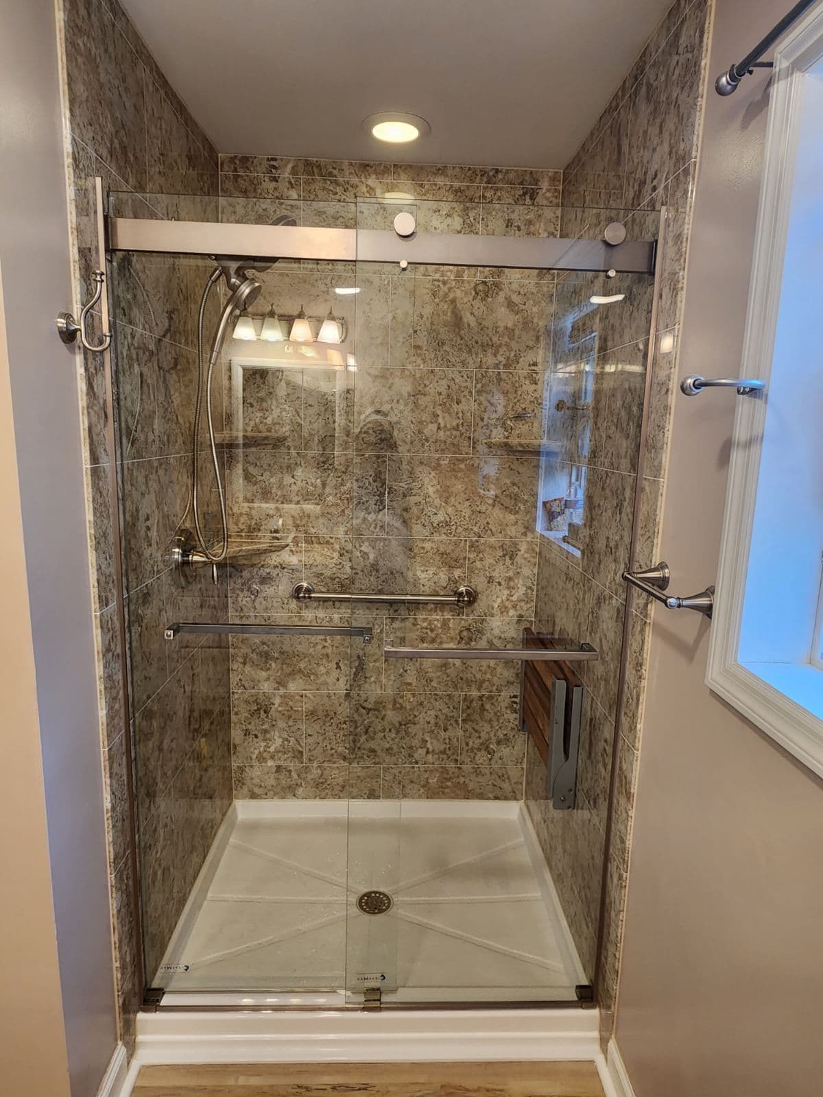 A walk-in shower with sliding glass doors and new brown marbled shower surround.