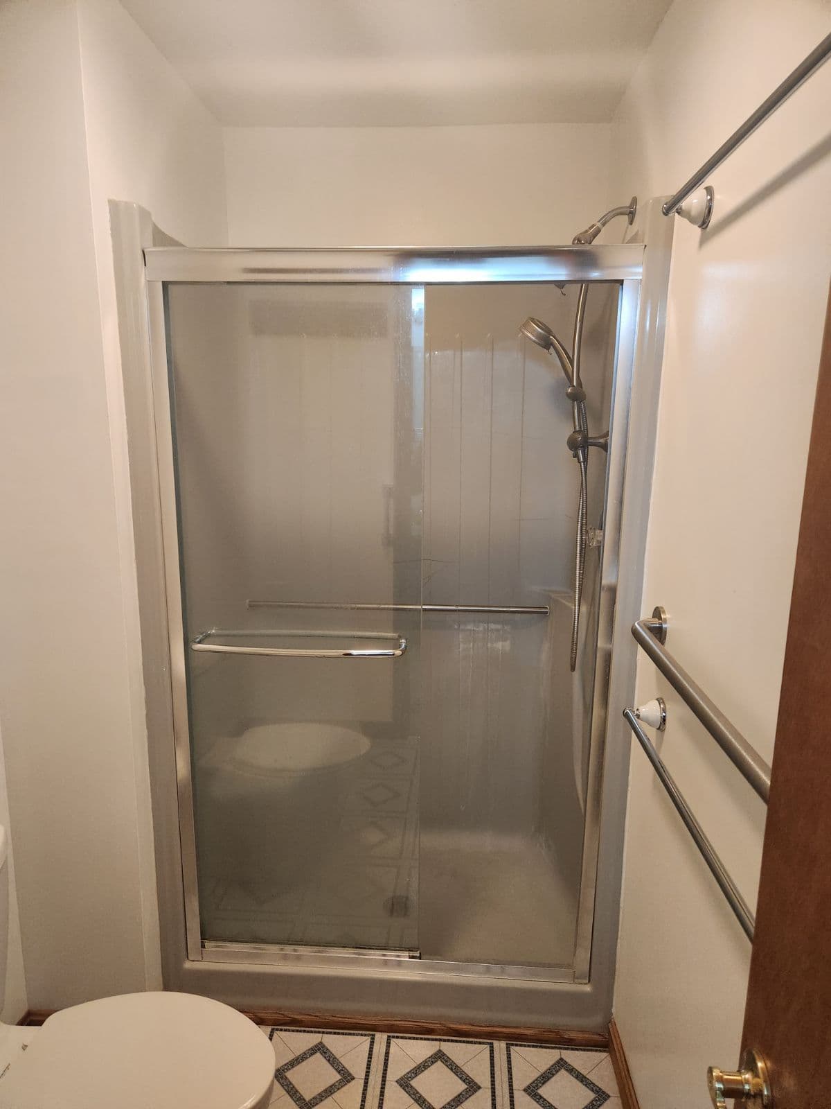 A dated walk-in shower stall with sliding glass door.