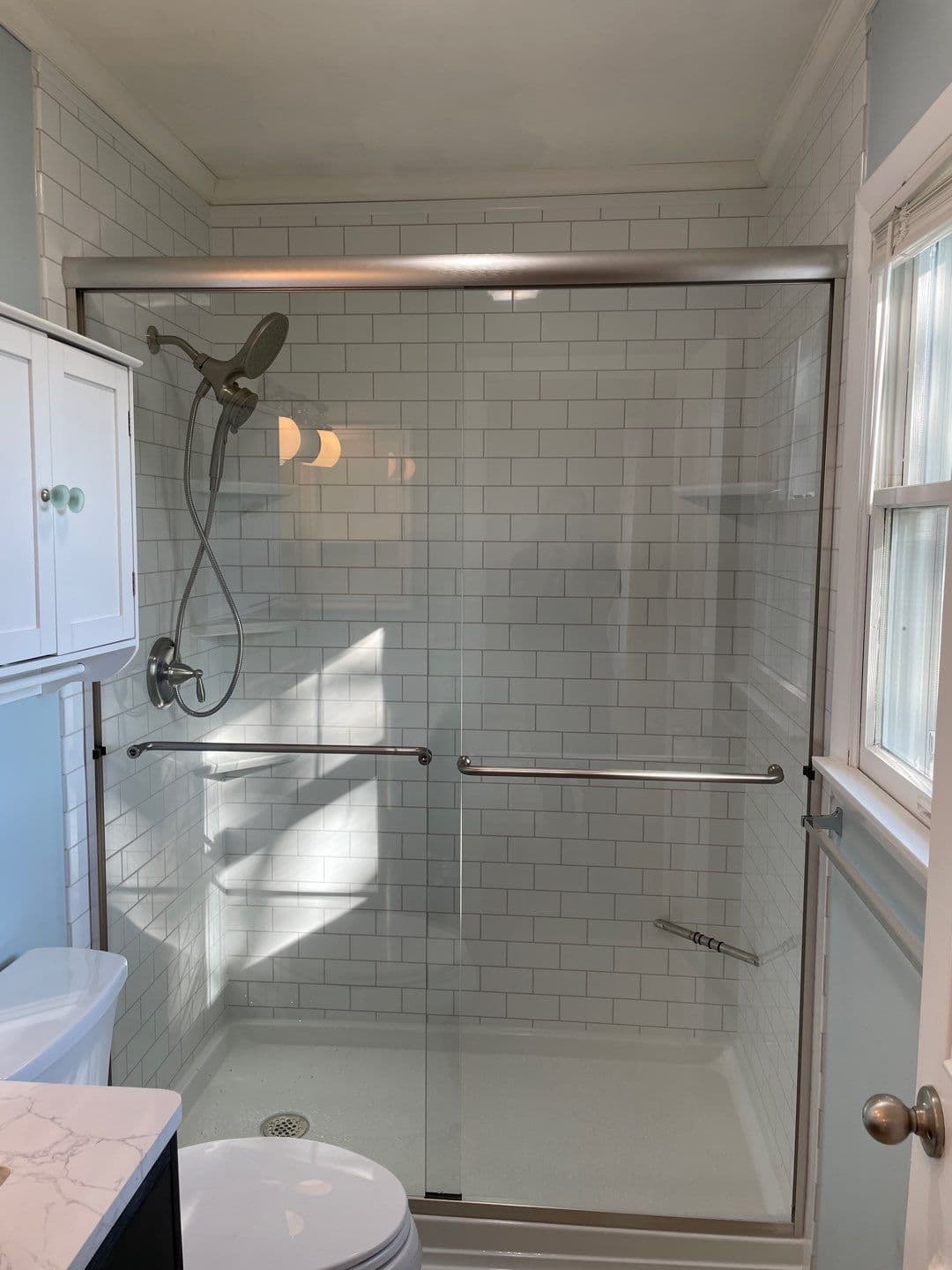 A walk-in shower with sliding glass doors and white tile patterned walls.