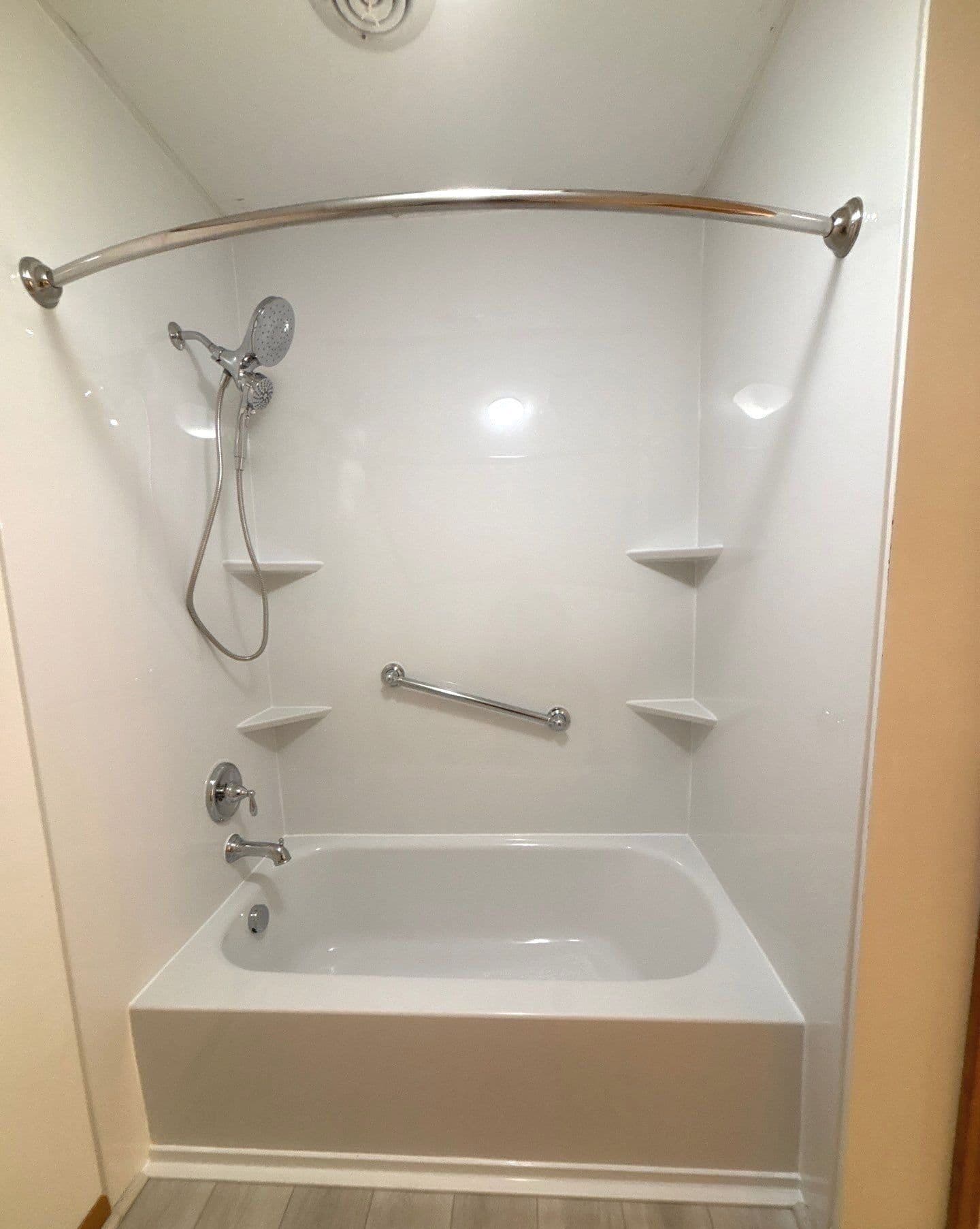 A combination shower tub with grab bar and corner shelves.