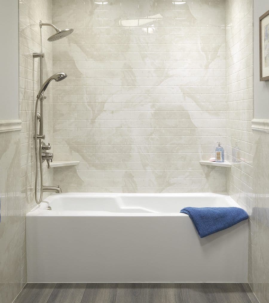 A combination white acrylic tub and shower with white tile walls and corner shelves.
