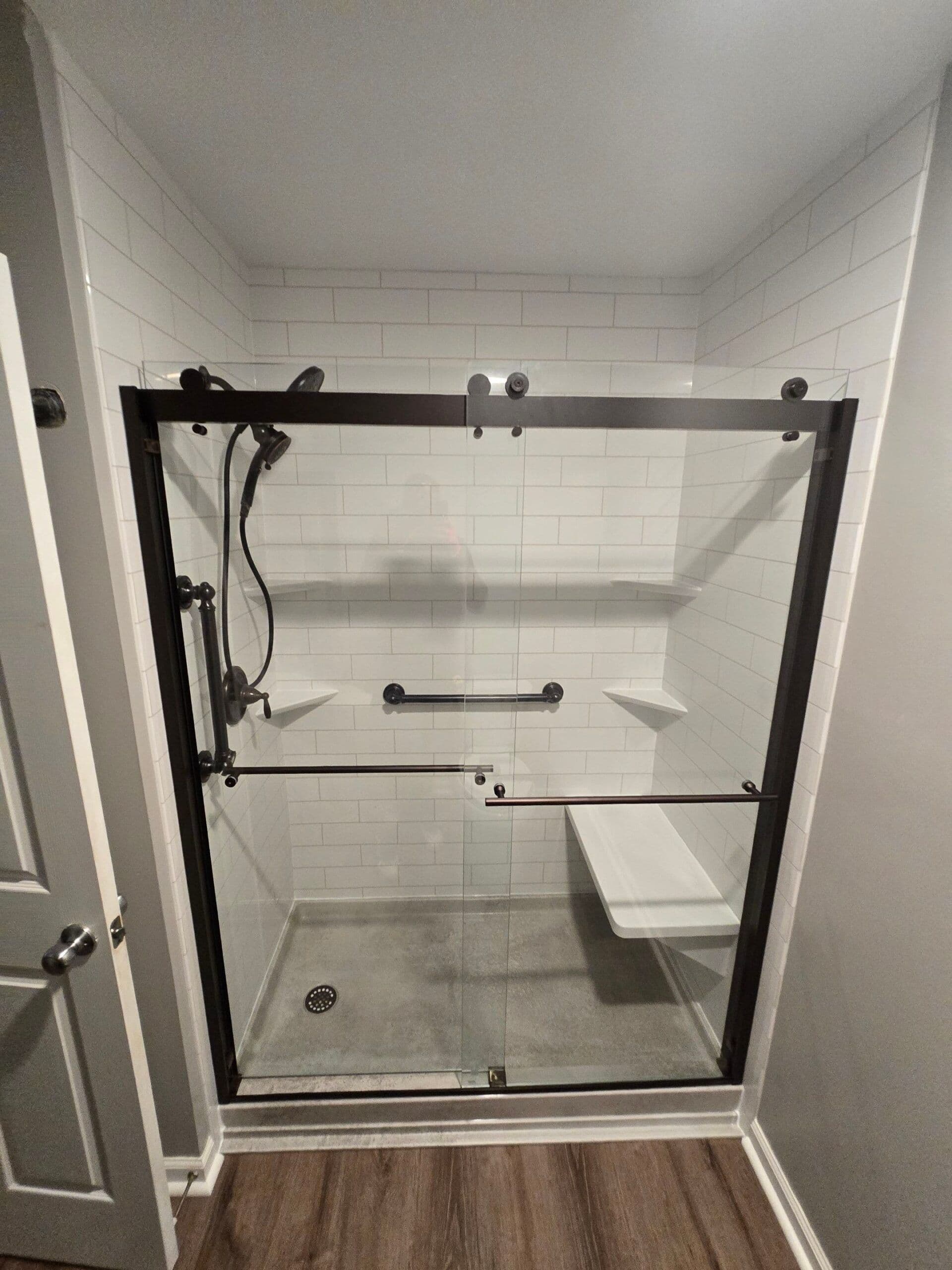 A converted walk-in shower with sliding glass doors, black fixtures, grab bar, and built-in bench seat.