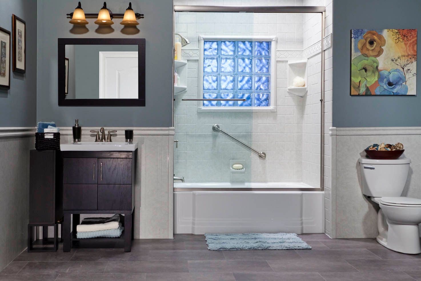 A blue-gray and white bathroom with a combination shower-tub with a window, sliding glass doors, and diagonal grab bar.