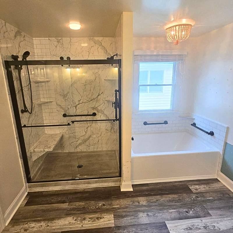 A walk-in shower with sliding glass doors, marbled walls, and grab bars on the left side, and a large soaking bathtub in an alcove on the right side of a bathroom.