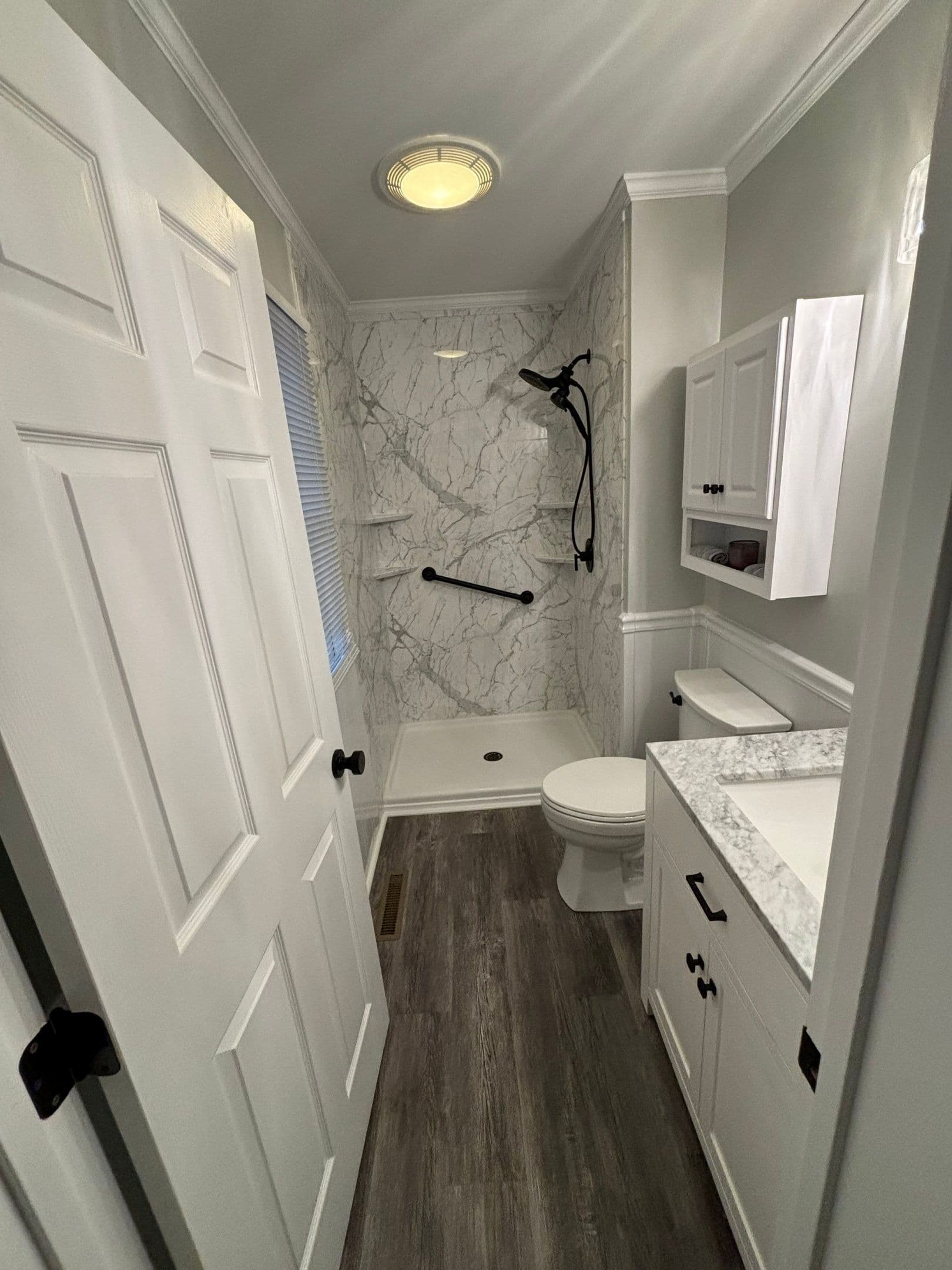 A walk-in shower with black fixtures, grab bar, and white and gray marbled walls.