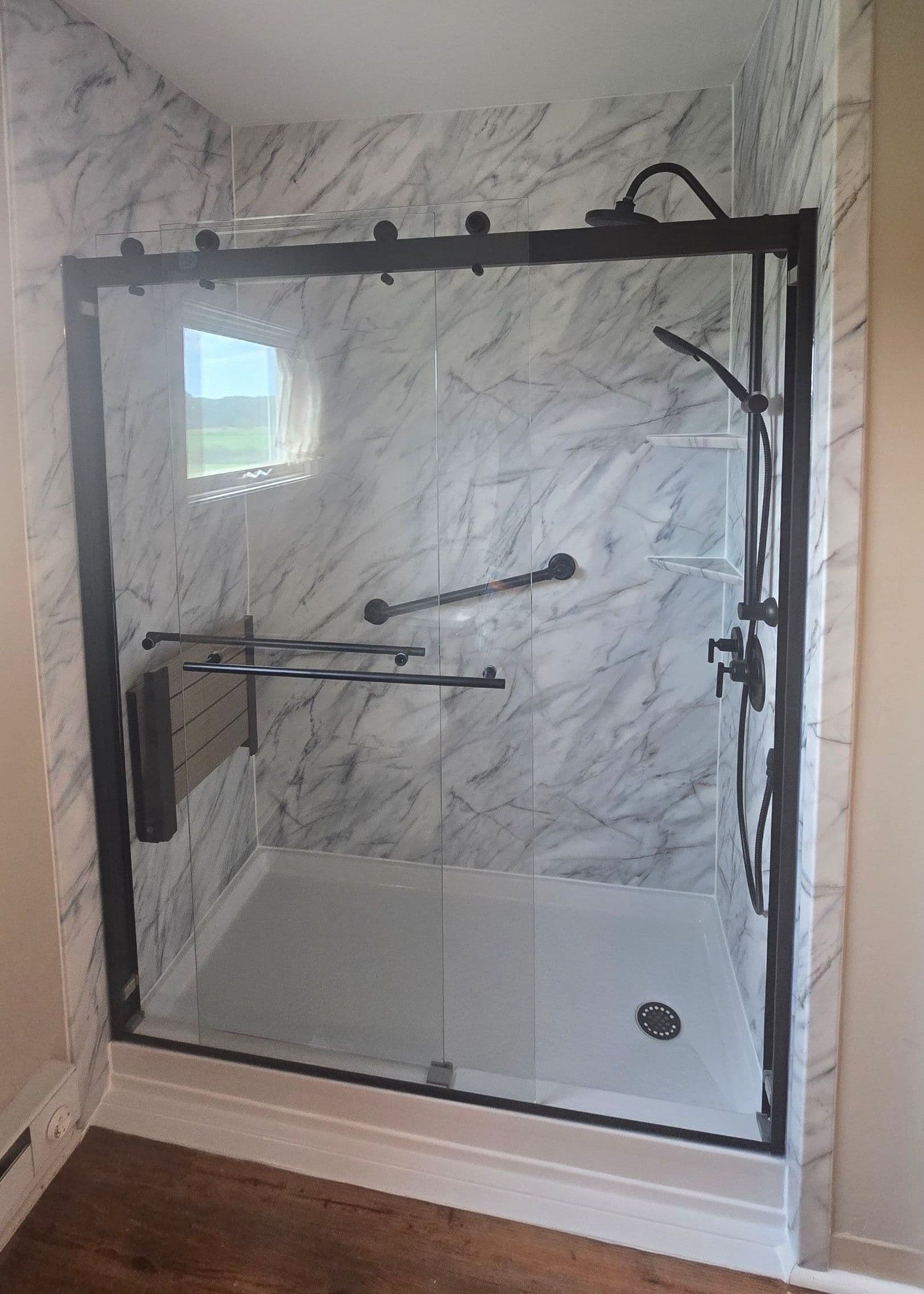 A walk-in shower with sliding glass doors, black fixtures, grab bar, and folding bench seat.