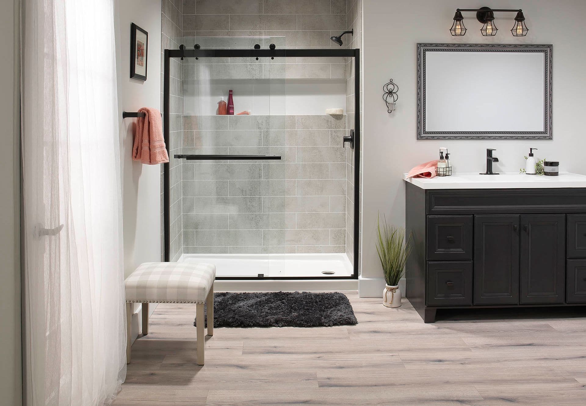 A walk-in shower with sliding glass doors, black fixtures, gray tile pattern walls, and a built-in storage caddy.
