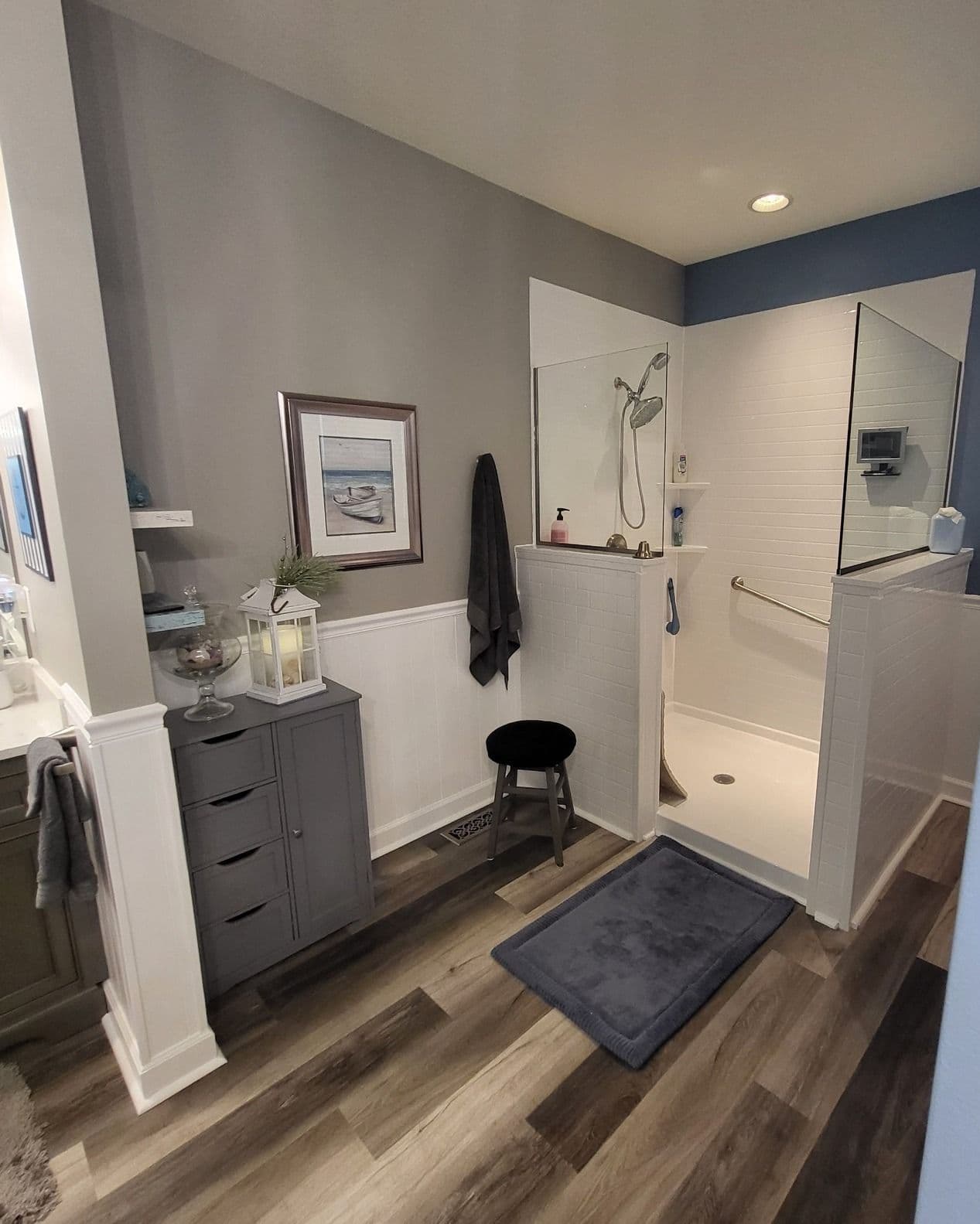 A walk-in shower in a gray and blue bathroom with glass partitions and white tile walls.
