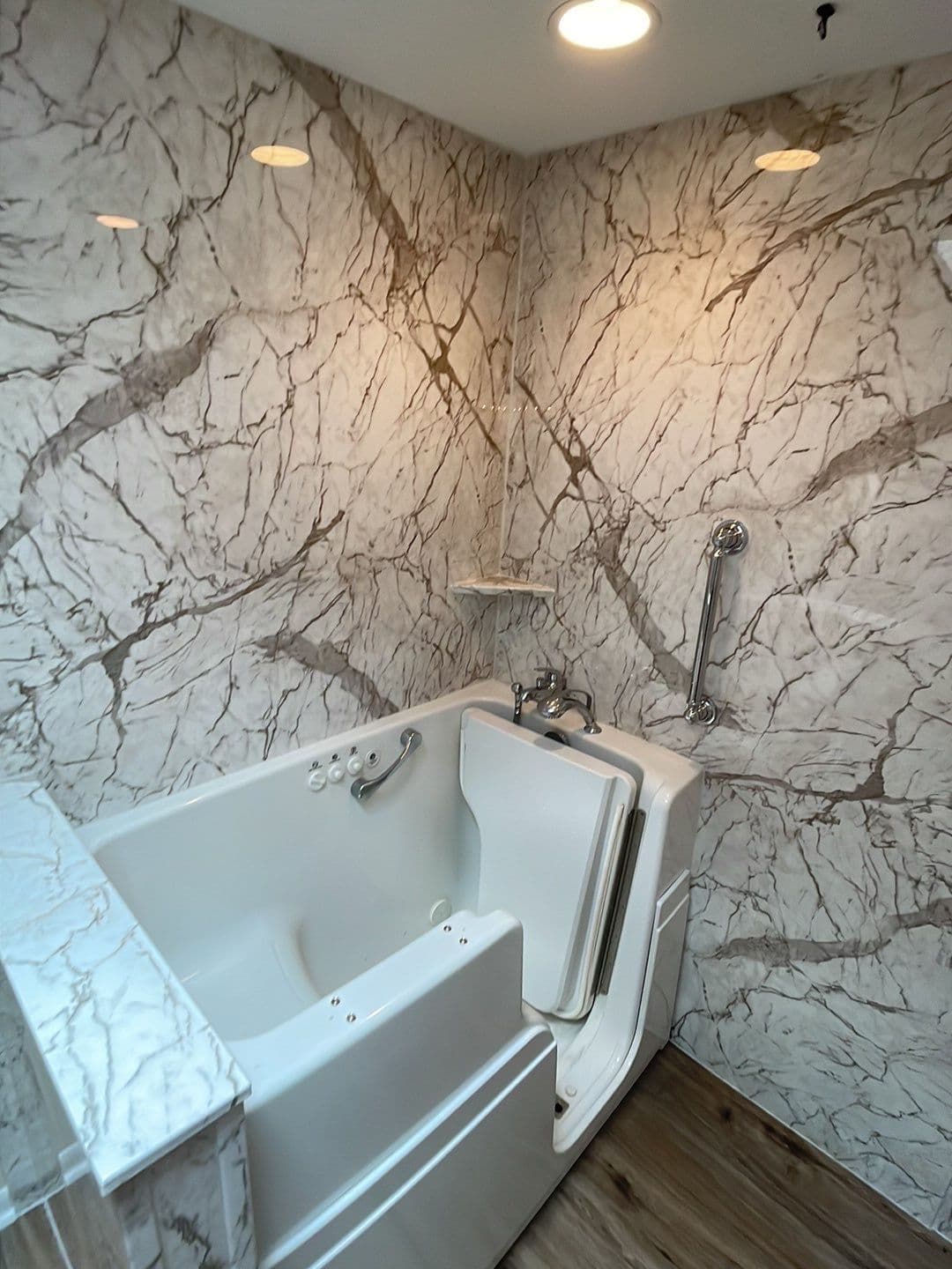 A walk-in bathtub with a vertical grab bar in a bathroom with marbled walls.